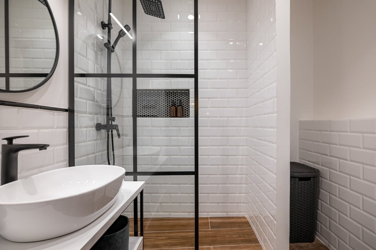Modern bathroom with glass shower enclosure, white subway tile walls, and wooden flooring