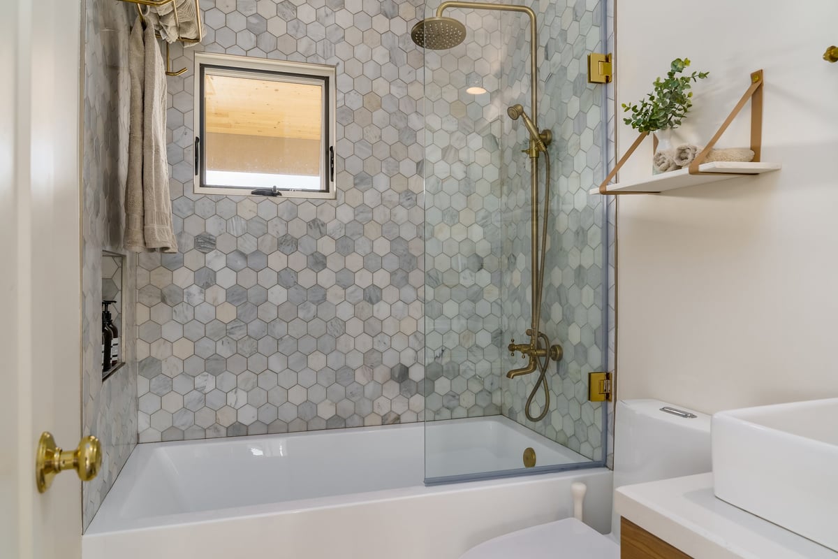 Modern white bathroom with shower tub and hexagonal tile and gold brass fixtures