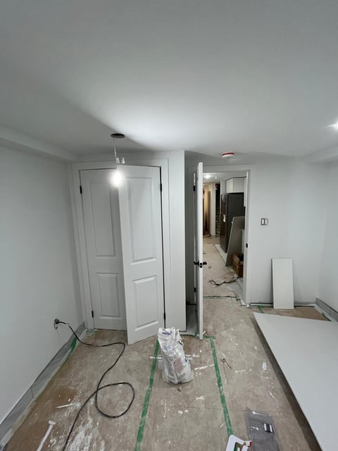 Interior room under renovation with white doors, exposed subfloor, construction equipment, and drop cloths