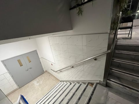Modern staircase with white marble tiles, metal railing, and gray upper walls with potted plants visible in background