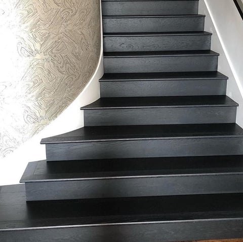 Dark wooden staircase ascending to the right with a beige patterned curved wall on the left and white trim