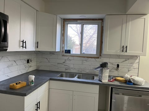 Modern kitchen with white cabinetry, dark countertops, white subway tile backsplash, and window overlooking outdoor trees