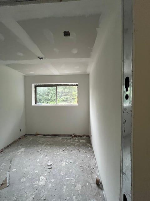 Unfinished interior room with white drywall walls, concrete floor, and a window overlooking greenery
