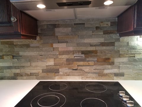 Modern kitchen with black electric cooktop and multicolored stone tile backsplash under recessed lighting