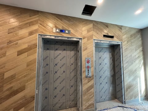 Two modern elevators with metal doors in a lobby with wood-textured walls and recessed ceiling lights