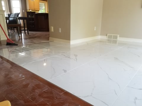 Large white marble tile floor installation in home interior with kitchen visible in background