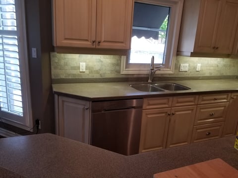 Kitchen countertop and sink area with wooden cabinets, green tile backsplash, stainless steel appliances, and window above sink