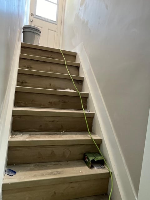 Wooden staircase with white walls and a yellow electrical cord running down the steps, leading to a door with window at the top