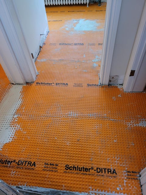 Orange Schluter-DITRA floor heating mat installed under doorways and hallway during renovation