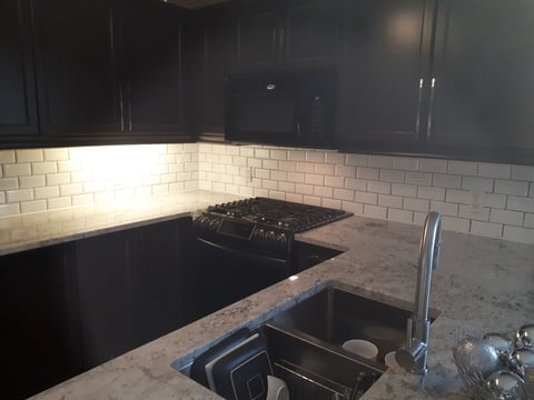 Modern kitchen with black cabinets, subway tile backsplash, gas cooktop, and marble countertops with stainless steel sink