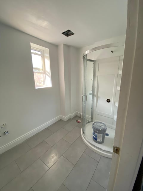Modern bathroom with white tiles, corner shower enclosure, small window, and minimalist decor
