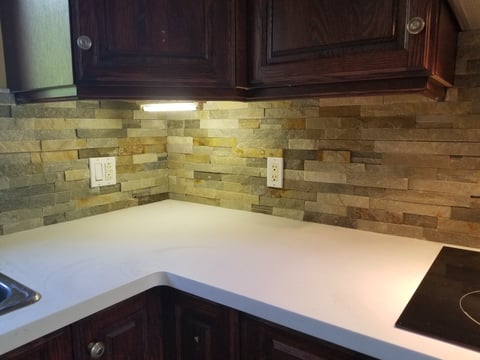 Modern kitchen counter with white quartz countertop, dark wood cabinets, and multi-colored stone tile backsplash with under-cabinet lighting