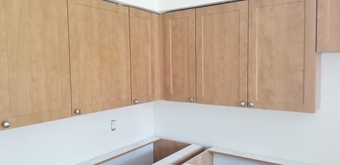 Unfinished wooden kitchen cabinets installed on white walls with open counter space below