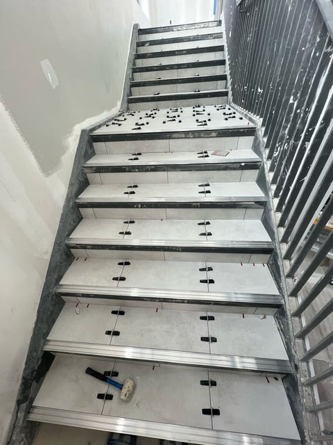 Interior staircase with metal handrail showing underfloor heating installation with black pipes and electrical conduit laid out on each step