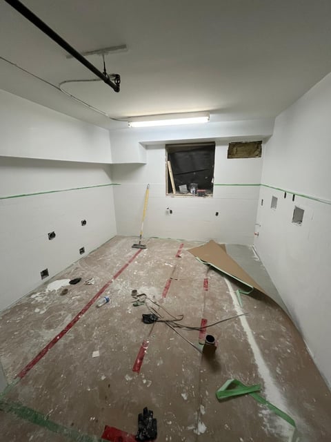 Interior room under renovation with white walls, marked floor layout lines, construction debris, exposed ceiling fixtures, and window opening