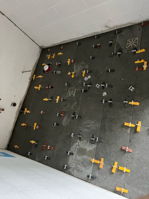 Dark wall with yellow and metal clamps mounted in organized rows, used for construction or drywall installation