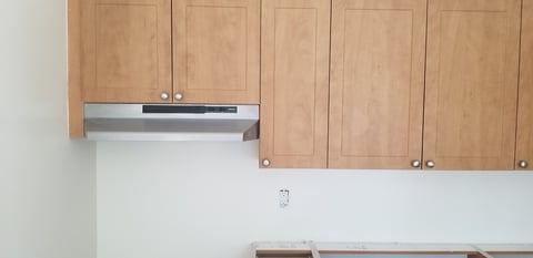Modern kitchen with light wood cabinets and stainless steel range hood mounted above white walls