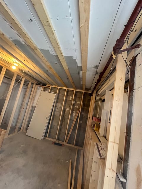 Interior of a basement or room under construction with exposed wooden studs, drywall, and lighting fixtures installed on the ceiling