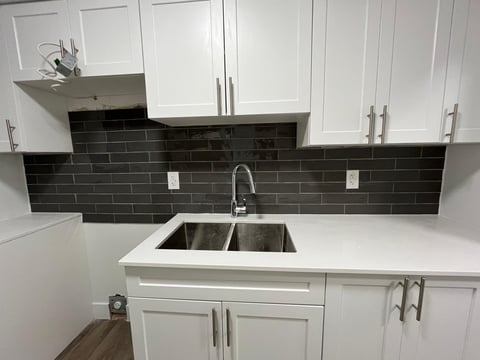 Modern kitchen with white cabinetry, stainless steel sink, black subway tile backsplash, and white countertop