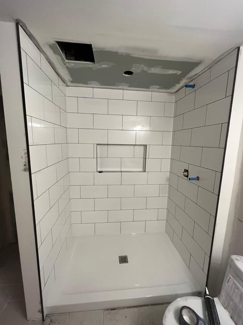 Modern bathroom shower enclosure with white subway tile walls, glass door, and white base under construction